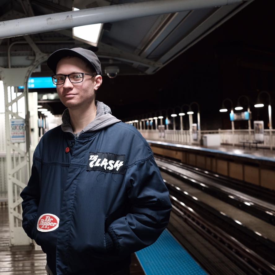 Davey facing the camera and standing on an above-ground train platform at night.